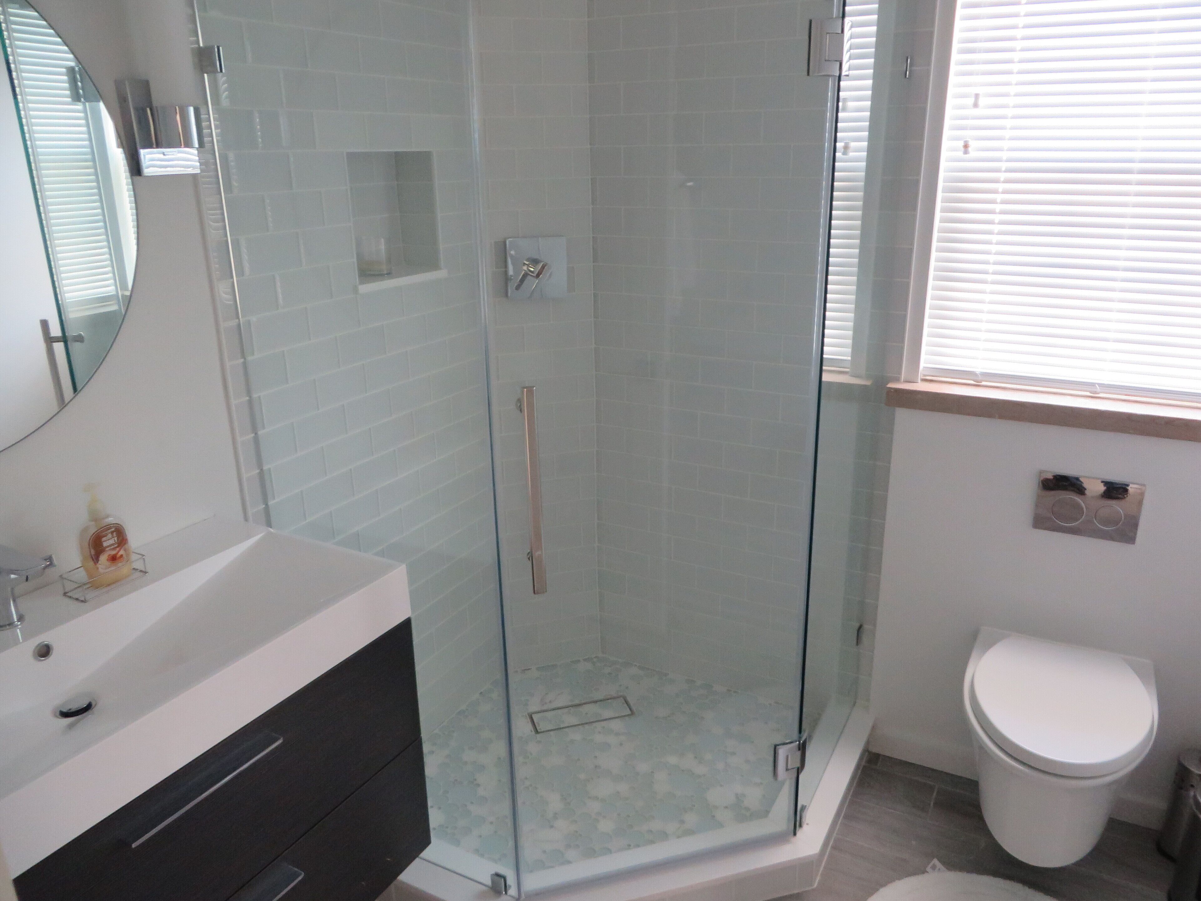 A modern bathroom with a glass-enclosed shower, a white sink with a mirror, and a toilet.