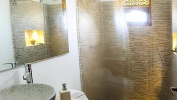 Un baño con lavamanos independiente, inodoro y ducha con mampara de vidrio.