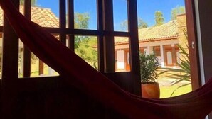 A window with a view of a building with a tiled roof and a hammock hanging across it. - Casa de las flores (Villa de Leyva)