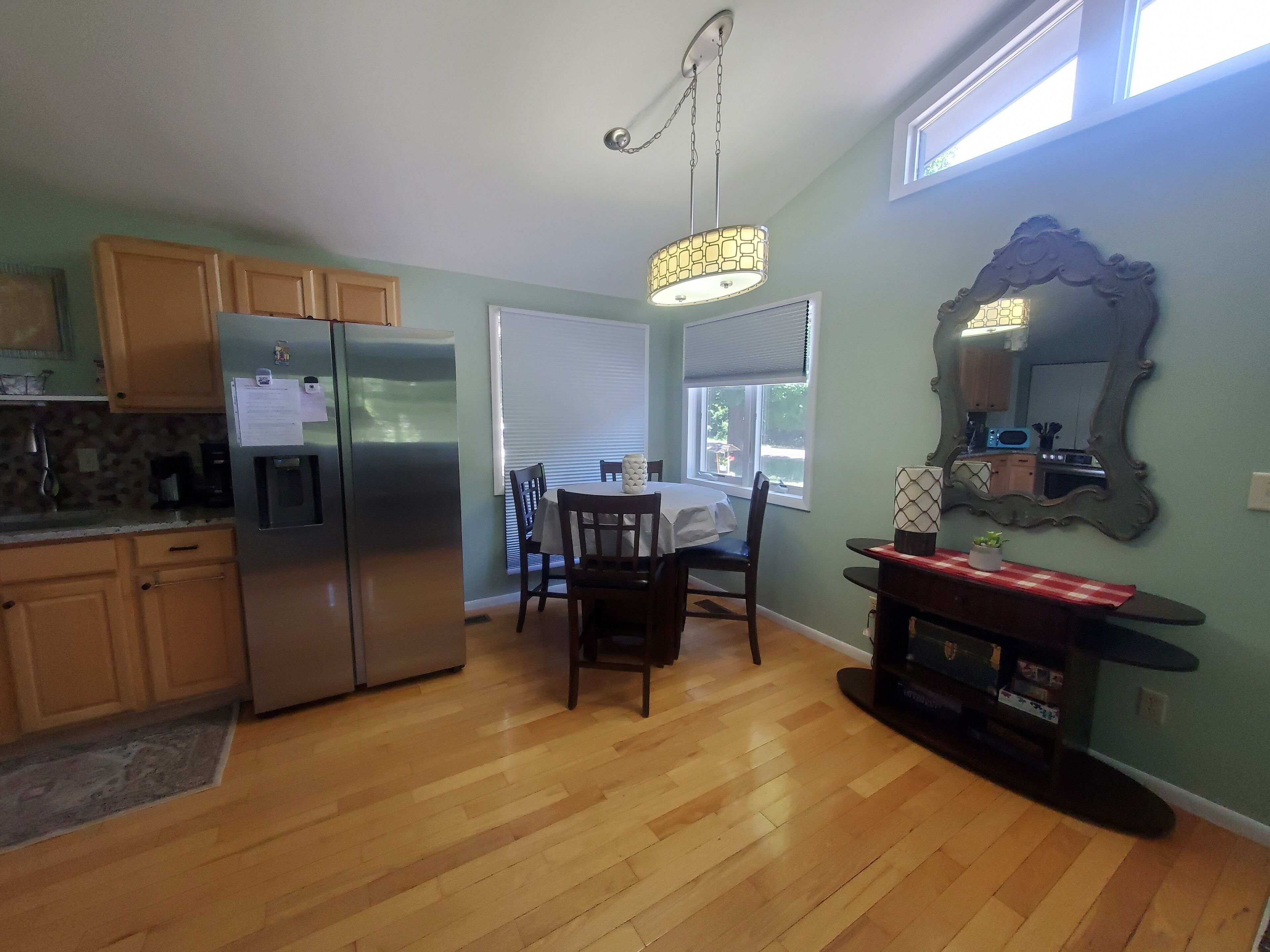 Una cocina moderna con armarios de madera, un refrigerador de acero inoxidable, una mesa de comedor con sillas y un espejo grande en la pared.