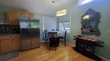 Una cocina moderna con armarios de madera, un refrigerador de acero inoxidable, una mesa de comedor con sillas y un espejo grande en la pared.