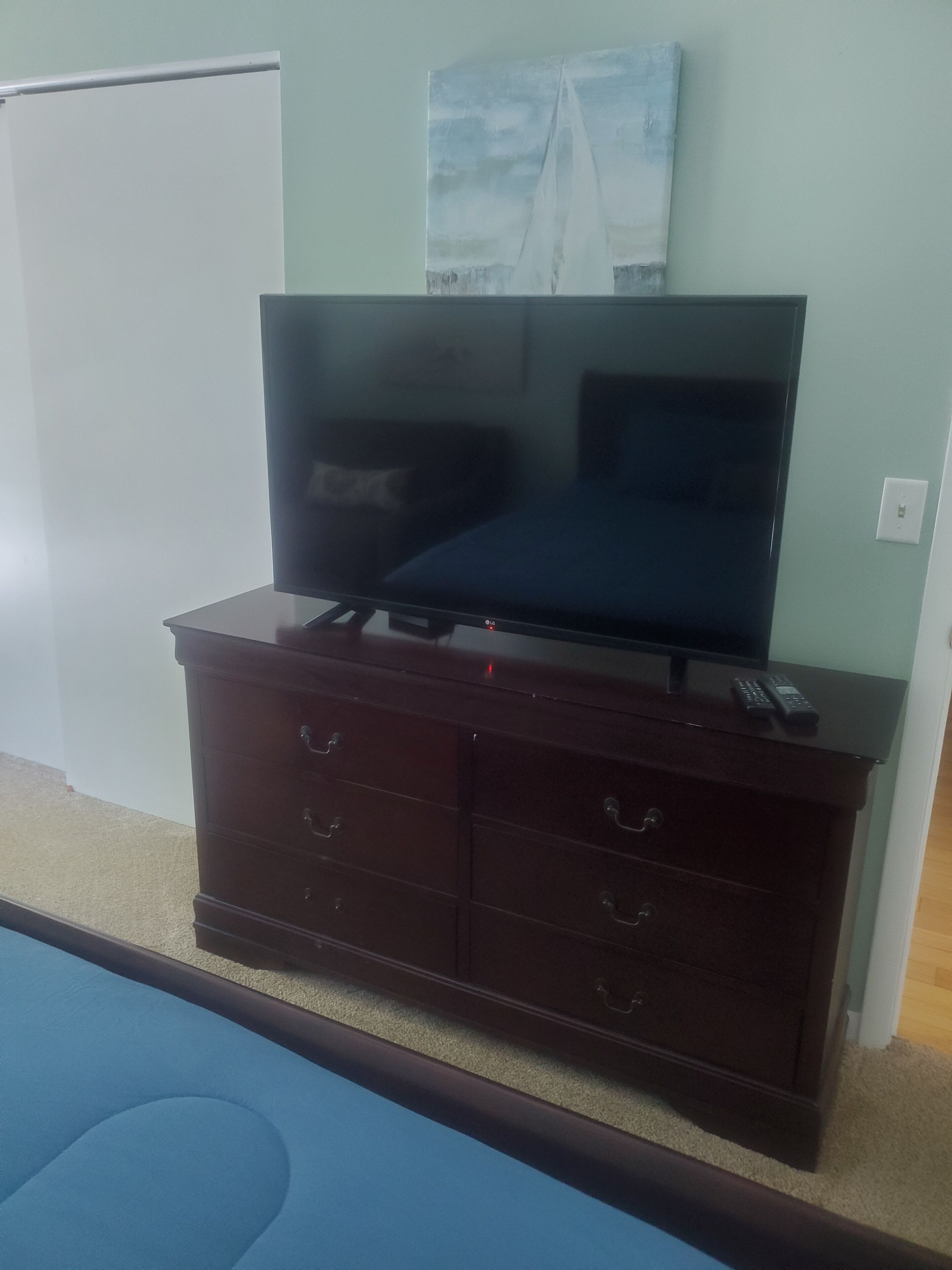 Un mueble bajo de madera oscura con un televisor de pantalla plana, un control remoto y un cuadro en la pared.