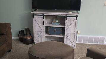 A living room with a flat-screen TV on a wooden entertainment unit, two brown sofas, and a beige ottoman.