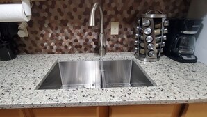 Una cocina con un lavamanos de acero inoxidable, una cafetera y un estante para especias.