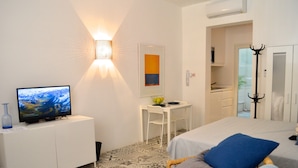 Ett hotellrum med en säng, ett skrivbord med en stol, en tv och en väggmonterad lampa.