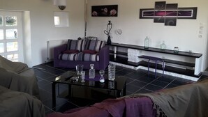 Ein Wohnzimmer mit einer Couch, einem Couchtisch und einer Bank. Auf der Bank liegen Dekorationen und an der Wand hängt eine Lampe.