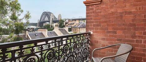 A balcony with a wrought iron railing, a wicker chair, and a view of a bridge and buildings.