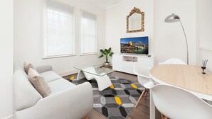Una sala de estar moderna con un sofá, una mesa de centro de vidrio, una mesa de comedor y un televisor.