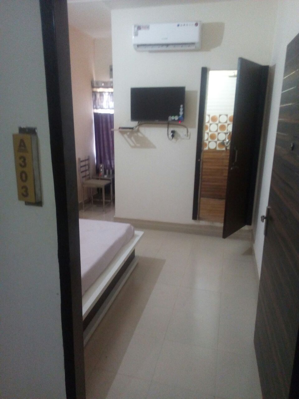 A hotel room with a bed, a TV mounted on the wall, and an air conditioning unit.