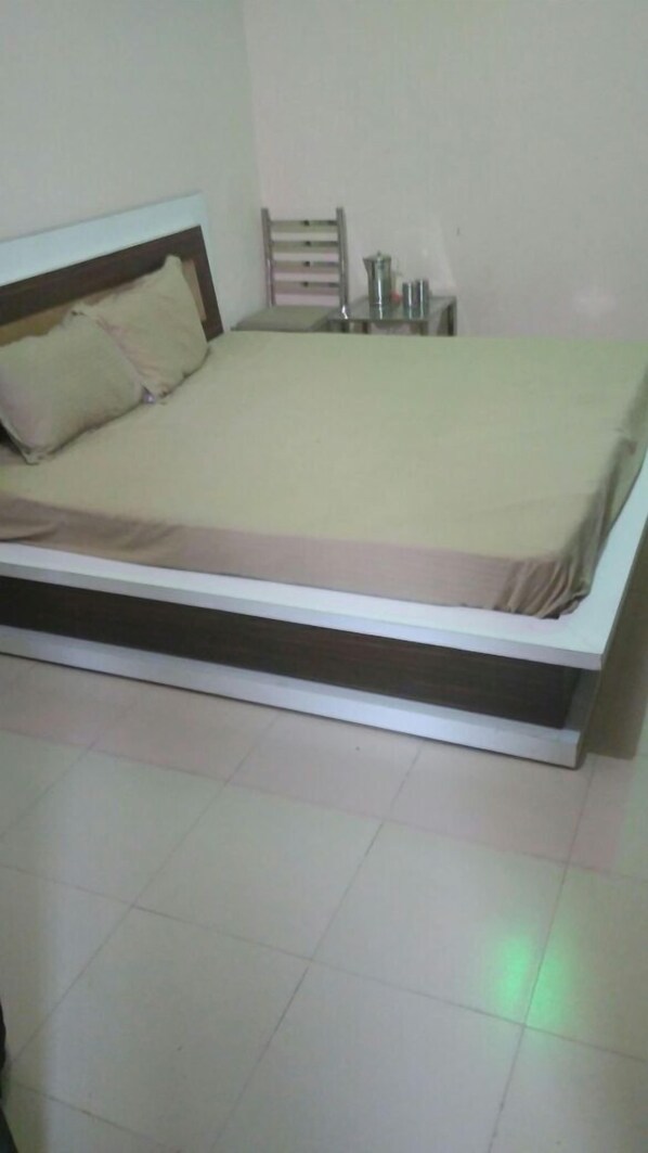 Habitación individual con una cama de madera, una mesita de noche con lámpara y una pequeña estantería.