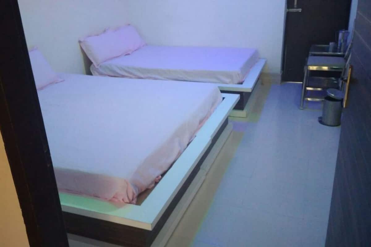 Un pasillo estrecho con dos camas individuales, cada una con una almohada y una mesita de noche. Se observa un cesto de basura a la derecha.