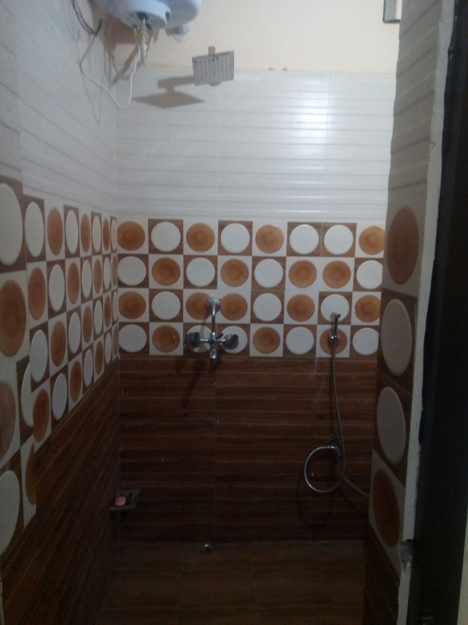 Ein Badezimmer mit Holzboden, Duschbereich und einer gefliesten Wand mit kreisförmigen Mustern.