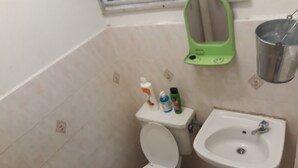 Ein kleines Badezimmer mit Toilette, Waschbecken und einem grünen Reinigungseimer.