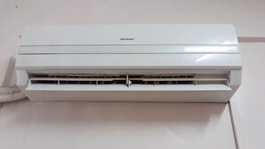 Eine weiße Klimaanlage mit dem Markenname "SHARP" obenauf.