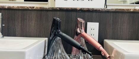 A bathroom with a mirror, a ReFa sign, two hair dryers, and a power outlet.