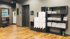 Un hall d’hôtel avec un plancher en bois, un distributeur automatique, un comptoir d’accueil et des étagères remplies de serviettes pliées.