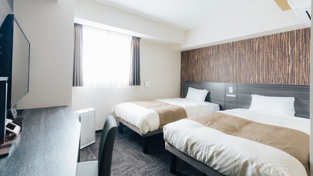 Une chambre d’hôtel avec deux lits, un bureau avec un ordinateur et une grande fenêtre.