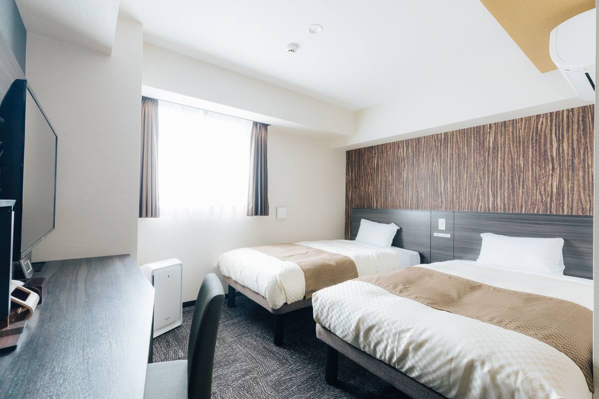 Ein Hotelzimmer mit zwei Betten, einem Schreibtisch mit Computer und einem großen Fenster.