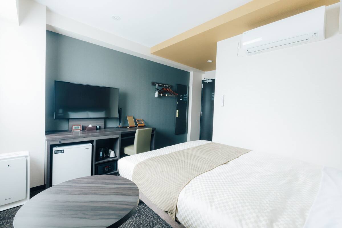 Ein Hotelzimmer mit Bett, Schreibtisch, Fernseher, kleinem Kühlschrank und Kleiderhaken.
