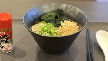 Una ciotola di ramen con scalogni e alghe, una bottiglia di condimento rosso e bacchette su un tavolo.
