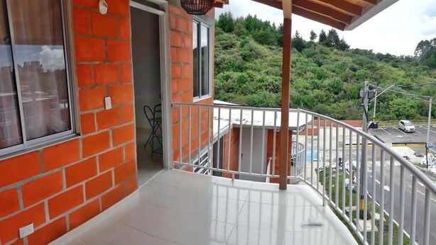 A balcony with a white railing, a brick wall, and a view of a road and greenery. - Come to Rionegro, Come to Life (Rionegro)