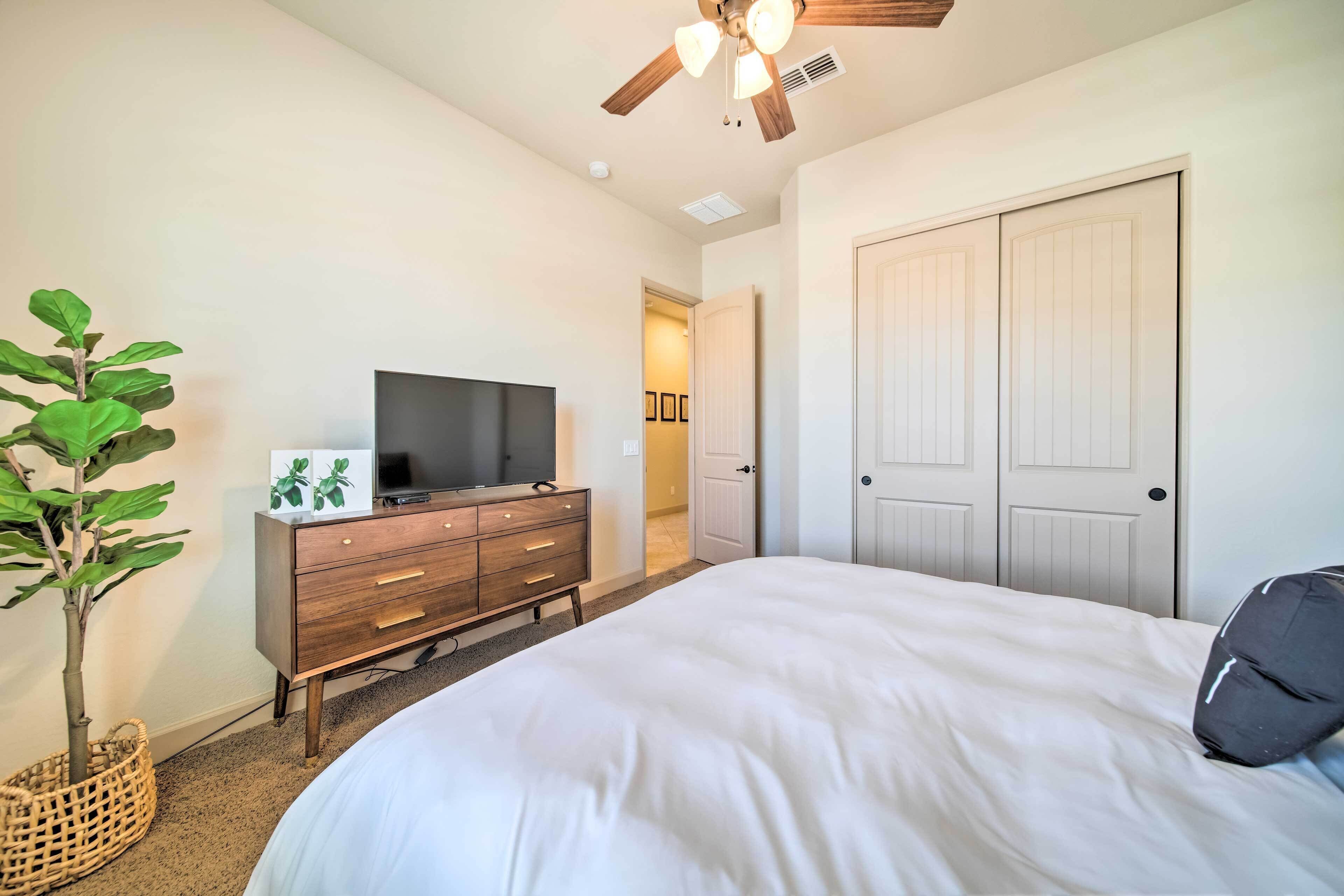 A bedroom with a bed, a dresser, a television, a ceiling fan, and a door.