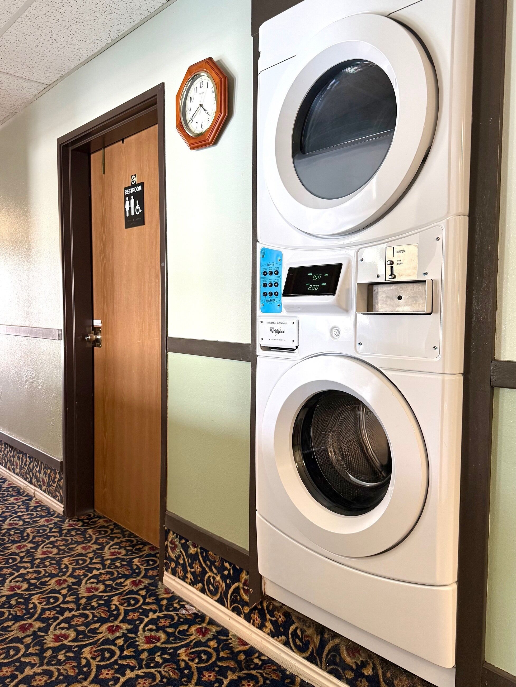 A hotel room with a washing machine, a clock, and a sign indicating a restroom.