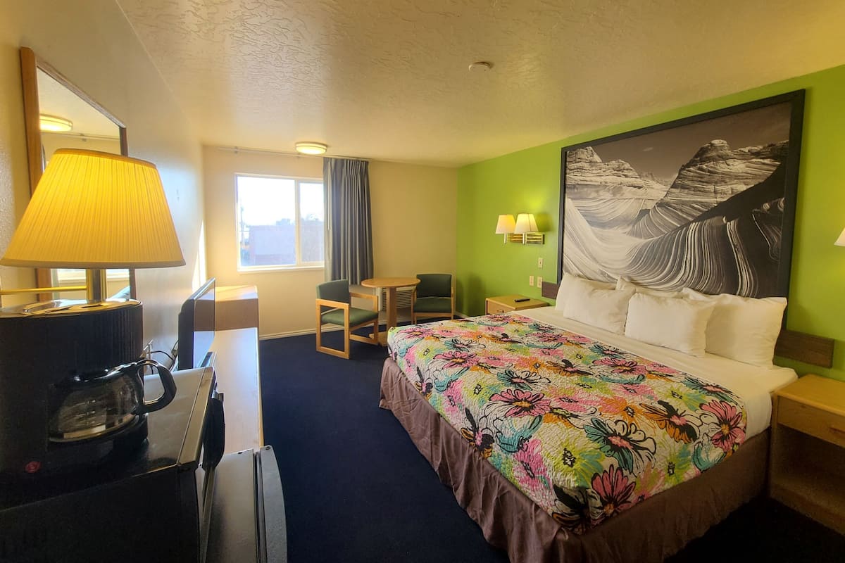 Habitación de hotel con cama, escritorio con lámpara, silla, mesita y un cuadro en la pared.