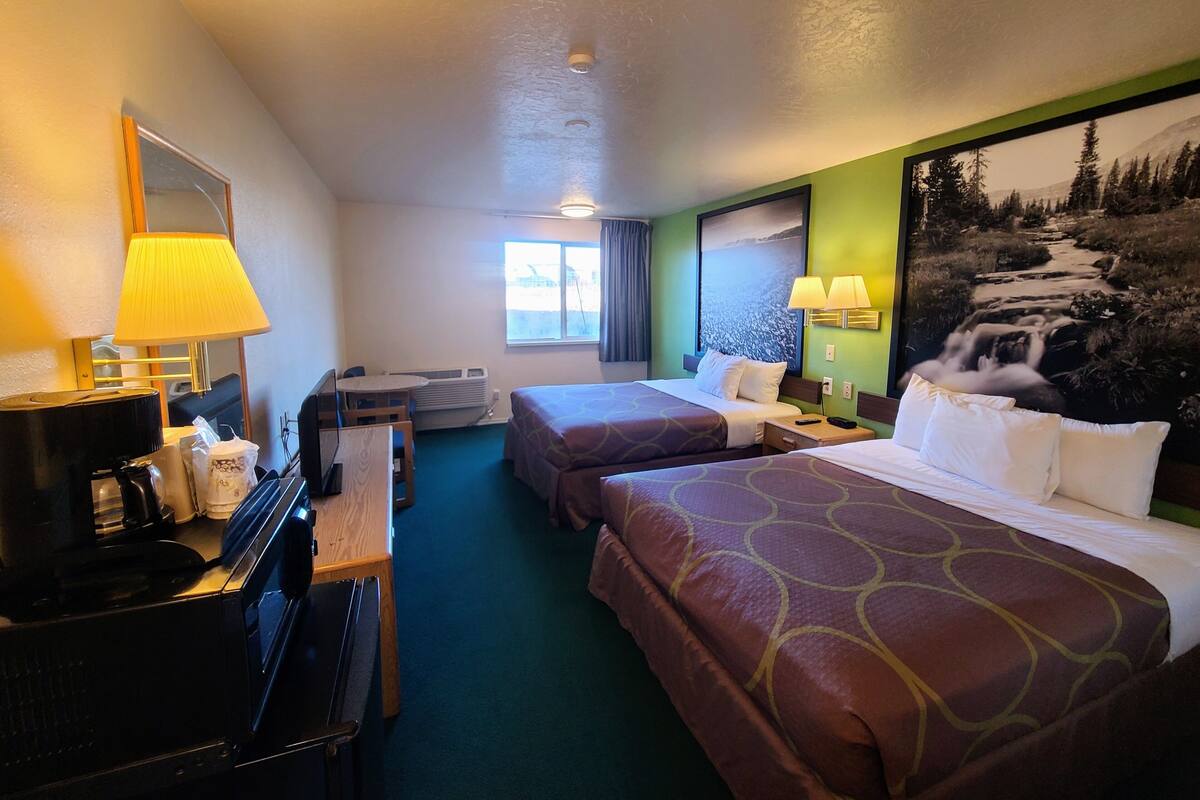 Habitación de hotel con dos camas, un escritorio con computadora, televisor y una ventana grande.
