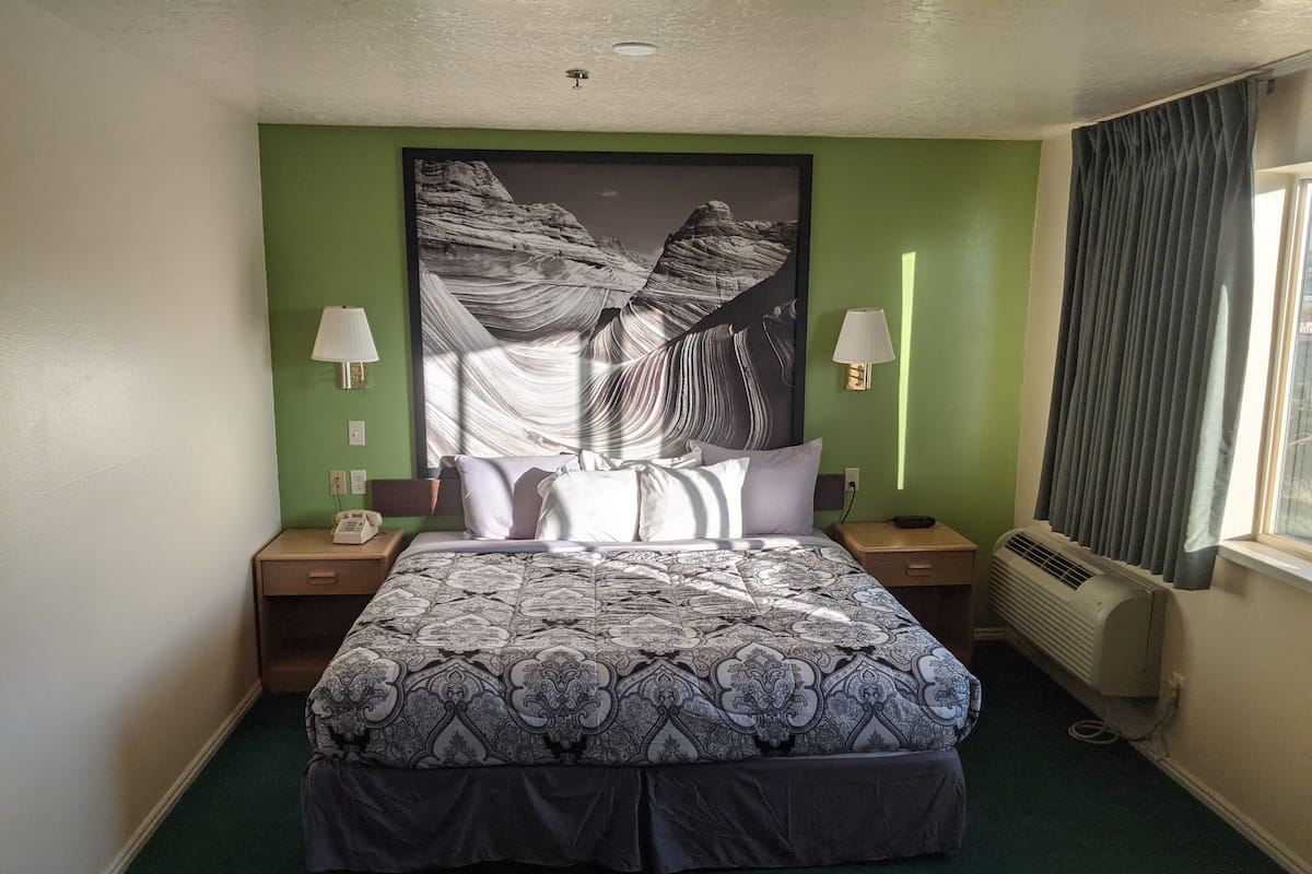 Una habitación de hotel con una cama grande, dos mesitas de noche, un teléfono, una lámpara de pared y un ventanal con cortinas.