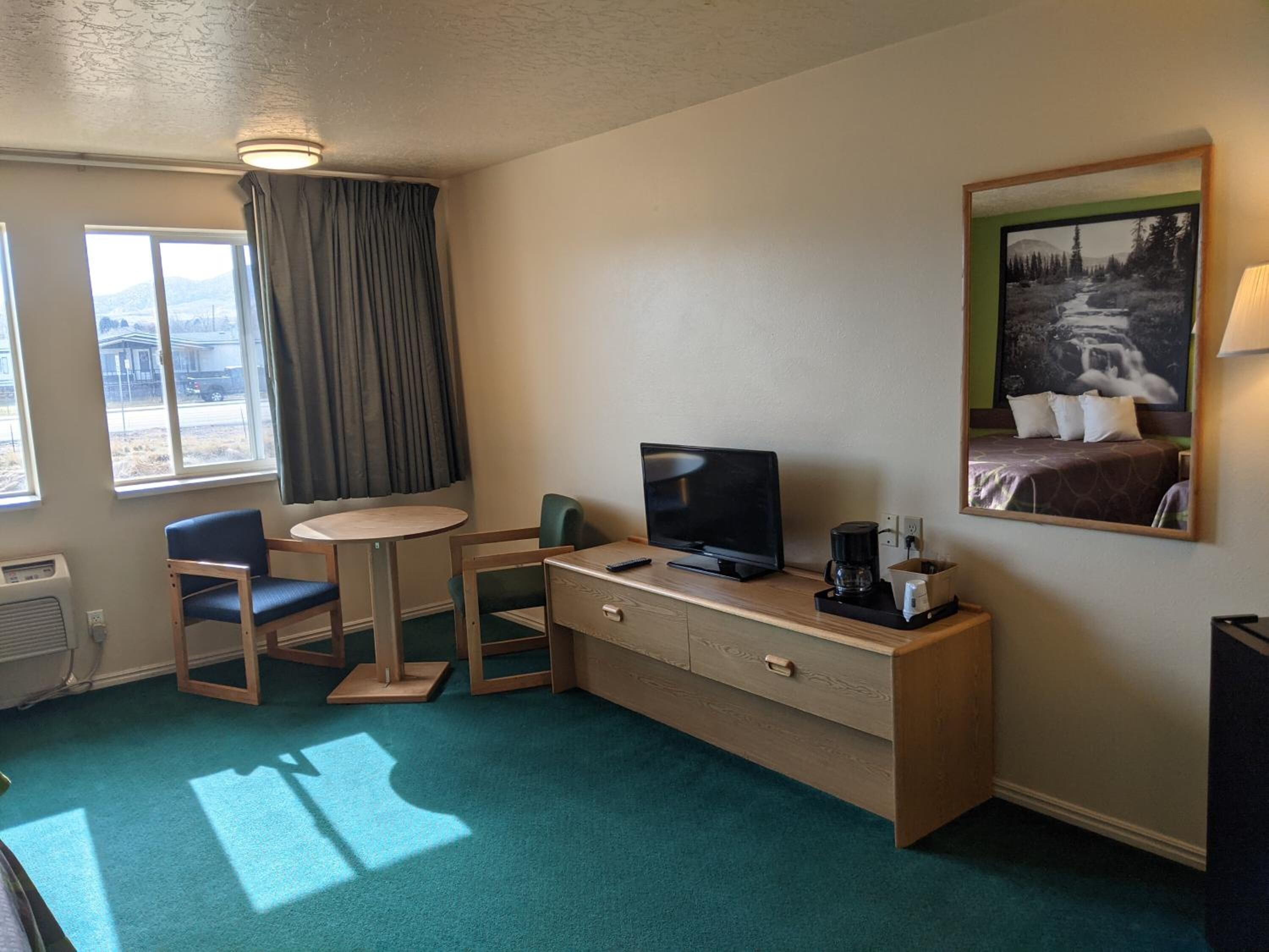 A hotel room with a desk, a television, a coffee maker, a chair, and a bed with a painting above it.
