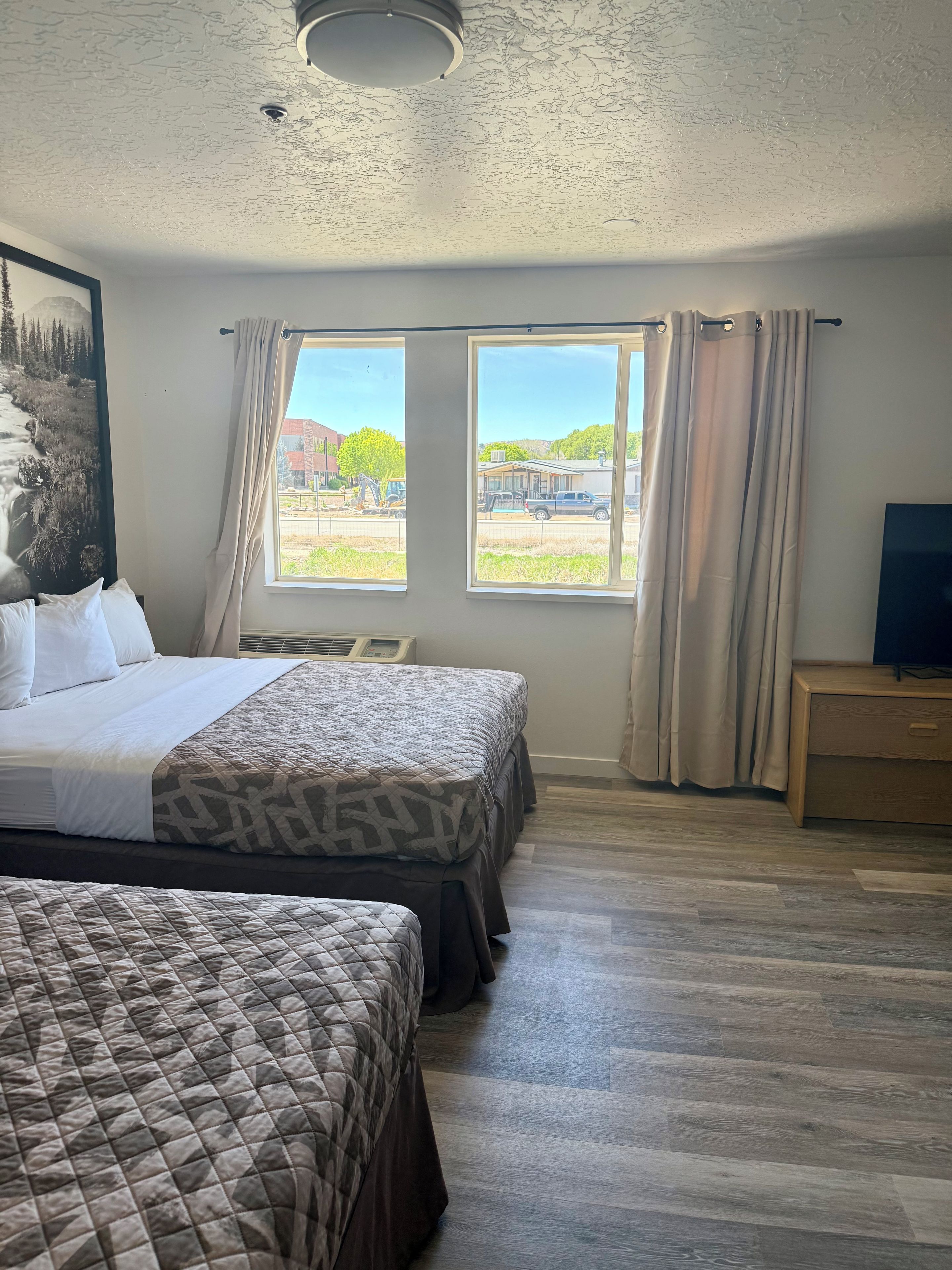 Habitación de hotel con dos camas, un ventanal con cortinas, un televisor de pantalla plana y un cuadro en la pared.