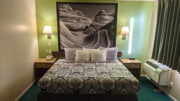Habitación de hotel con una cama grande, dos mesitas de noche, un teléfono, aire acondicionado instalado en la pared y un cuadro grande enmarcado.