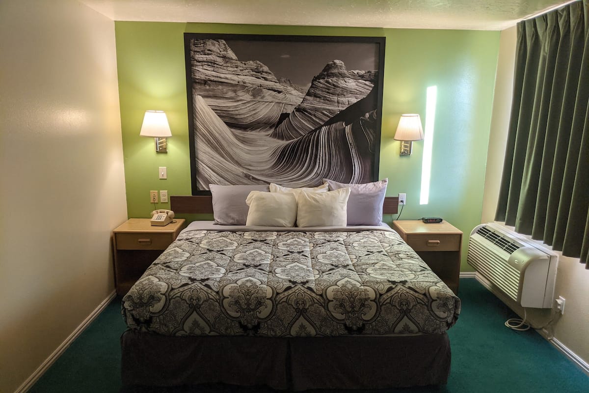 Habitación de hotel con una cama grande, dos mesitas de noche, un teléfono, aire acondicionado instalado en la pared y un cuadro grande enmarcado.