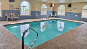 Una piscina interior con agua cristalina, rodeada de paredes con azulejos azules y ventanas de arco.