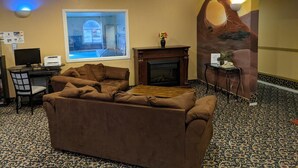 Un vestíbulo de hotel con un sofá grande, una chimenea, un escritorio con una computadora y un ventanal con vistas a una piscina.