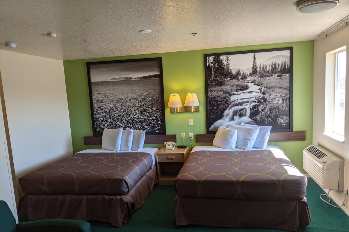 Habitación de hotel con dos camas, paredes verdes y dos grandes cuadros en blanco y negro con paisajes.