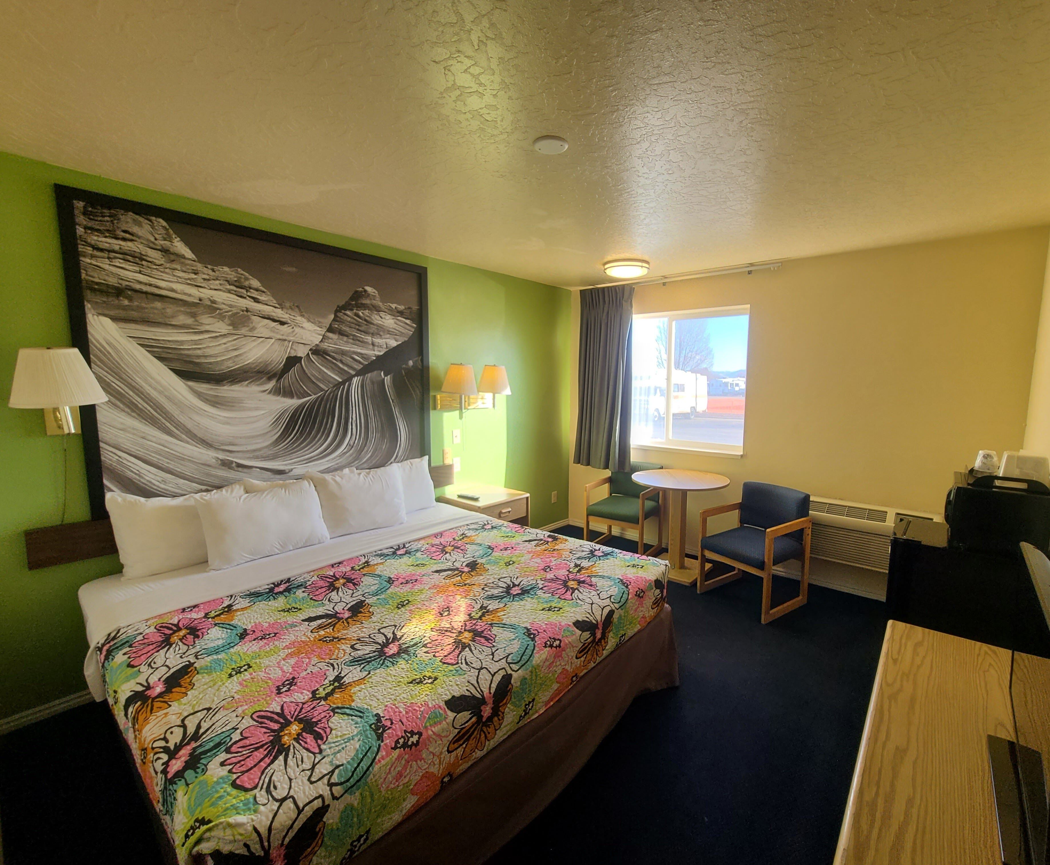 Une chambre d’hôtel avec un grand lit, un bureau, une chaise, une petite table et une fenêtre donnant sur un beau paysage.