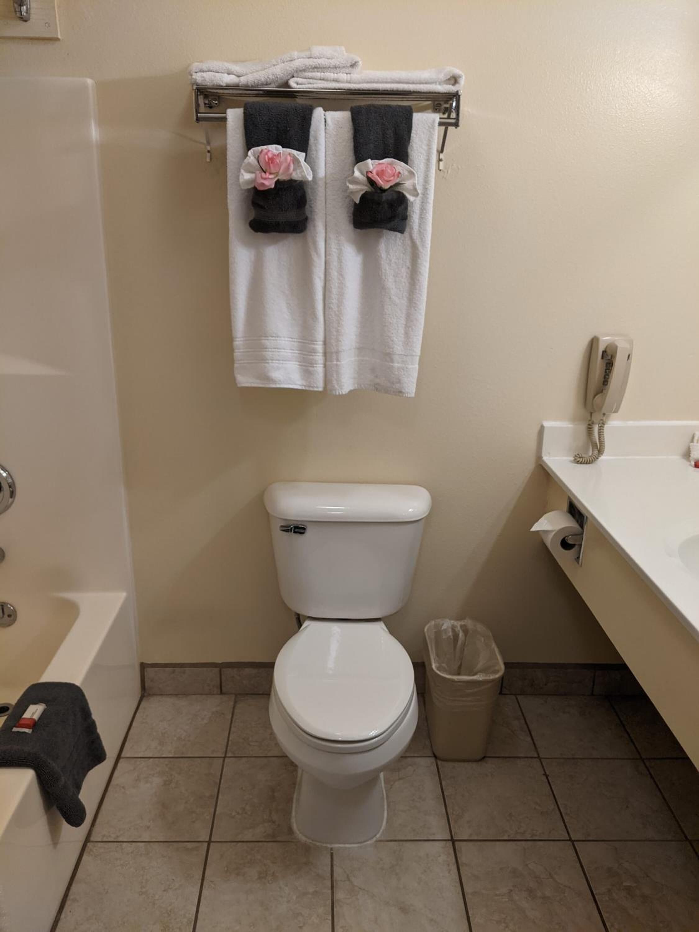 Un baño con inodoro, un cubo de basura, toallero con toallas, teléfono y bañera.