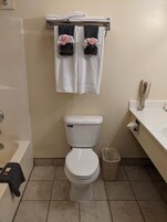 Un baño con inodoro, un cubo de basura, toallero con toallas, teléfono y bañera.