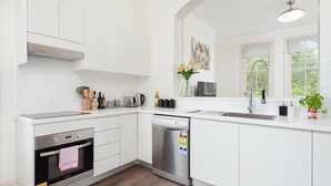 Eine moderne Küche mit weißen Schränken, einem eingebauten Backofen, einem Geschirrspüler und einem Fenster, das für natürliches Licht sorgt.