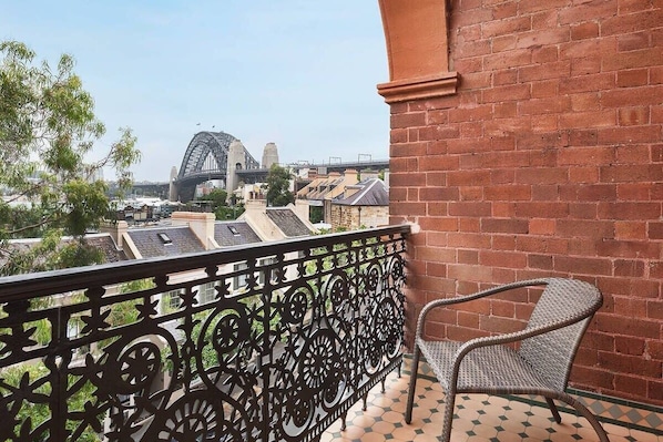 A balcony with a wrought iron railing, a wicker chair, and a view of a bridge and buildings.