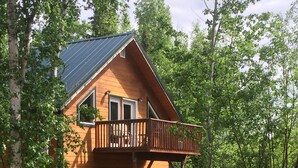 A wooden cabin with a balcony, surrounded by trees. - Misty Lake Carriage House (Wasilla)