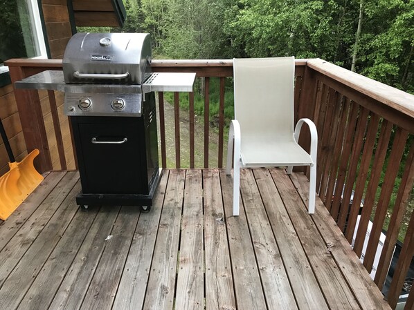A wooden deck with a black grill and a white chair.
