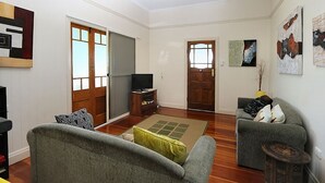 A living room with a sofa, a television, and a coffee table. There is a sliding door and a door leading to another room. - Billys Beach House, Elliott heads (ELLIOTT HEADS)