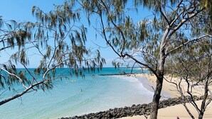 A beach with clear turquoise water, a rocky shoreline, and sparse vegetation. - Billys Beach House, Elliott heads (ELLIOTT HEADS)