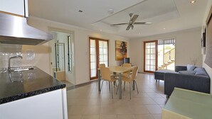 A modern kitchen with a stainless steel range hood, a dining area with a table and chairs, and a living area with a sofa and a TV. - Billys Beach House, Elliott heads (ELLIOTT HEADS)