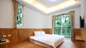 Quarto com cabeceira de madeira, cama com roupa de cama branca, mesa de cabeceira de madeira, janela com cortinas e varanda com vista para árvores.