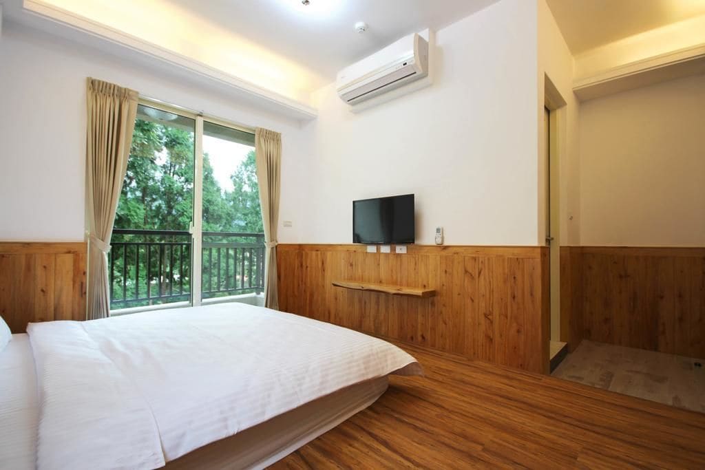 A bedroom with a bed, a TV mounted on the wall, and a window with curtains.