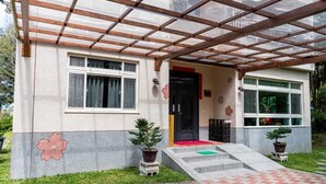 Um edifício com entrada coberta, um pequeno jardim com plantas em vasos e um caminho de tijolos que leva à entrada.